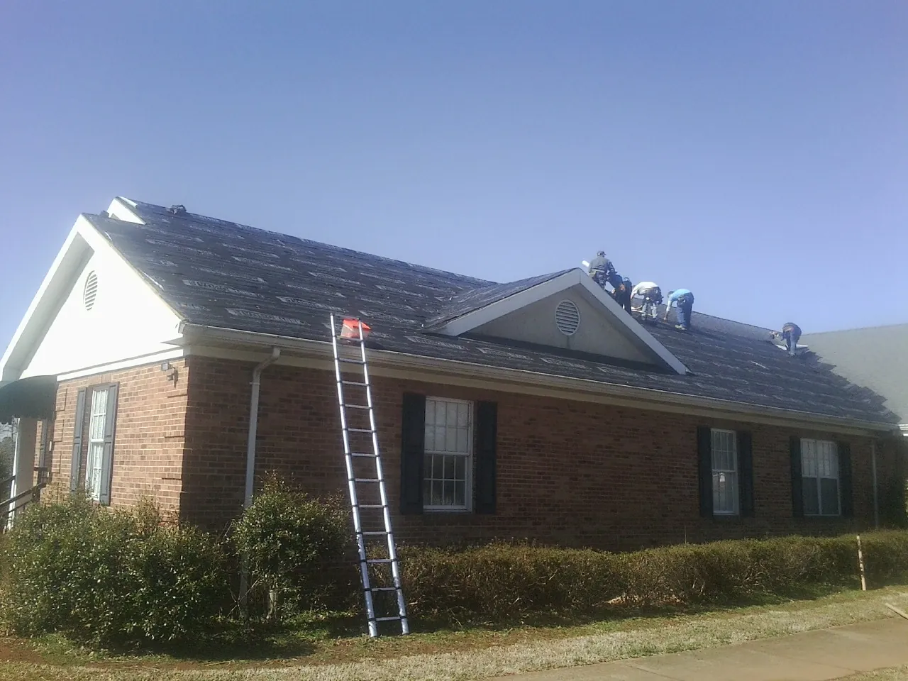 Crew tearing shingles off a brick ranch roof with a ladder set — Emergency Roof Repair work by our crew in Southfields