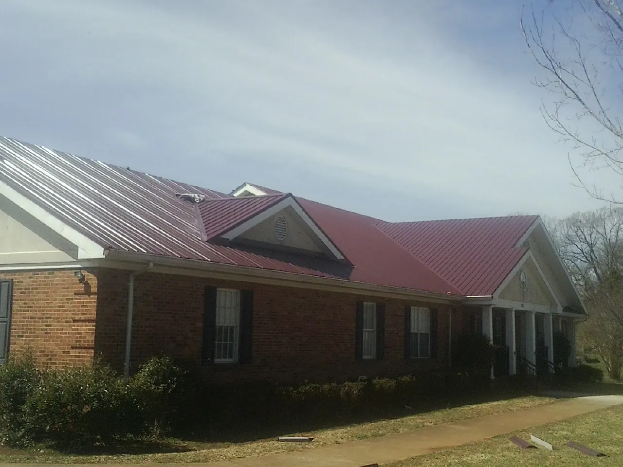 Red metal roof with gabled entries on a long brick building, from a Hail Damage Roof Repair job in Southfields